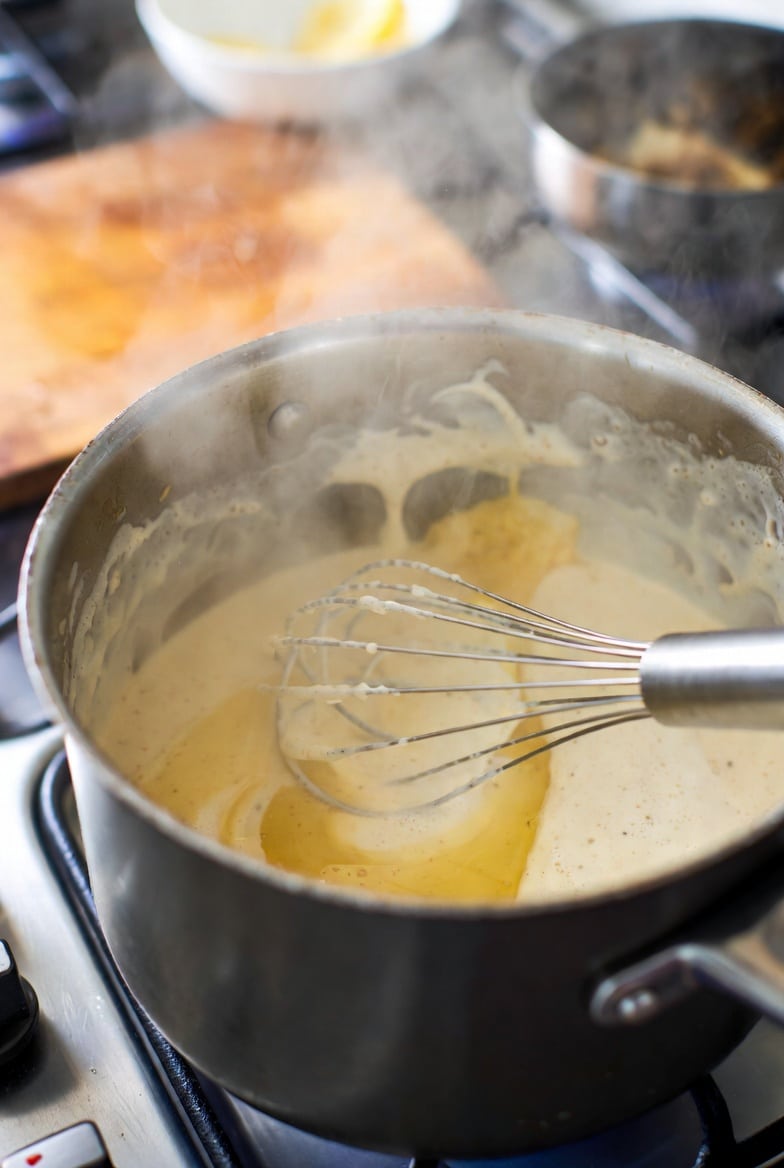 Dijon lemon cream sauce simmering in a saucepan with a whisk for a smooth creamy texture