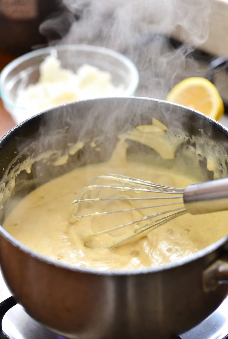 Creamy lemon sauce simmering gently in a saucepan with lemon and cream nearby