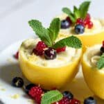 Creamy lemon posset in lemon shells topped with fresh berries and mint on a white plate